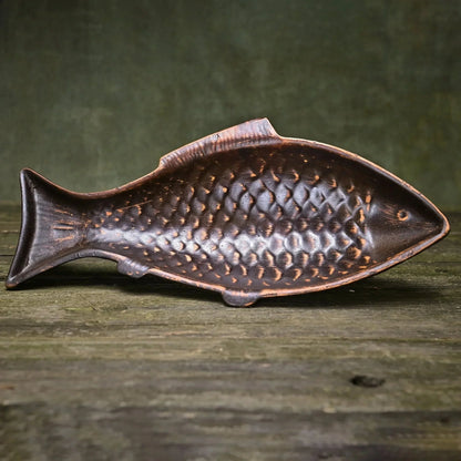 Handmade ceramic fish-shaped clay plate with textured scales on rustic wood surface