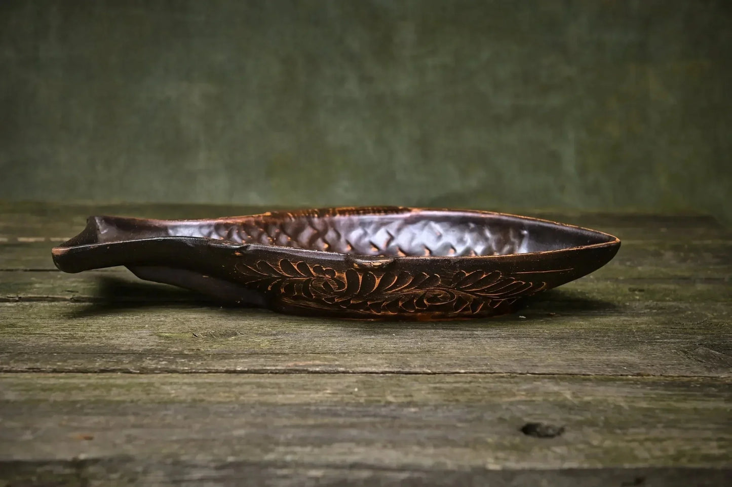 Handmade ceramic fish-shaped clay plate with carved scale and floral design on rustic wood