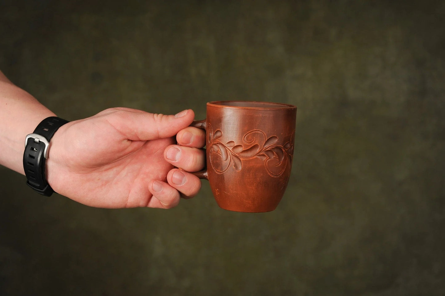 Hand holding a handmade red clay ceramic cup with engraved floral design, artisan crockery
