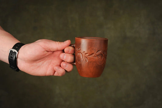 Hand holding a handmade red clay ceramic cup with engraved floral design, artisan crockery