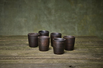 Set of six handmade ceramic shot glasses on rustic wood table, artisan clay homeware
