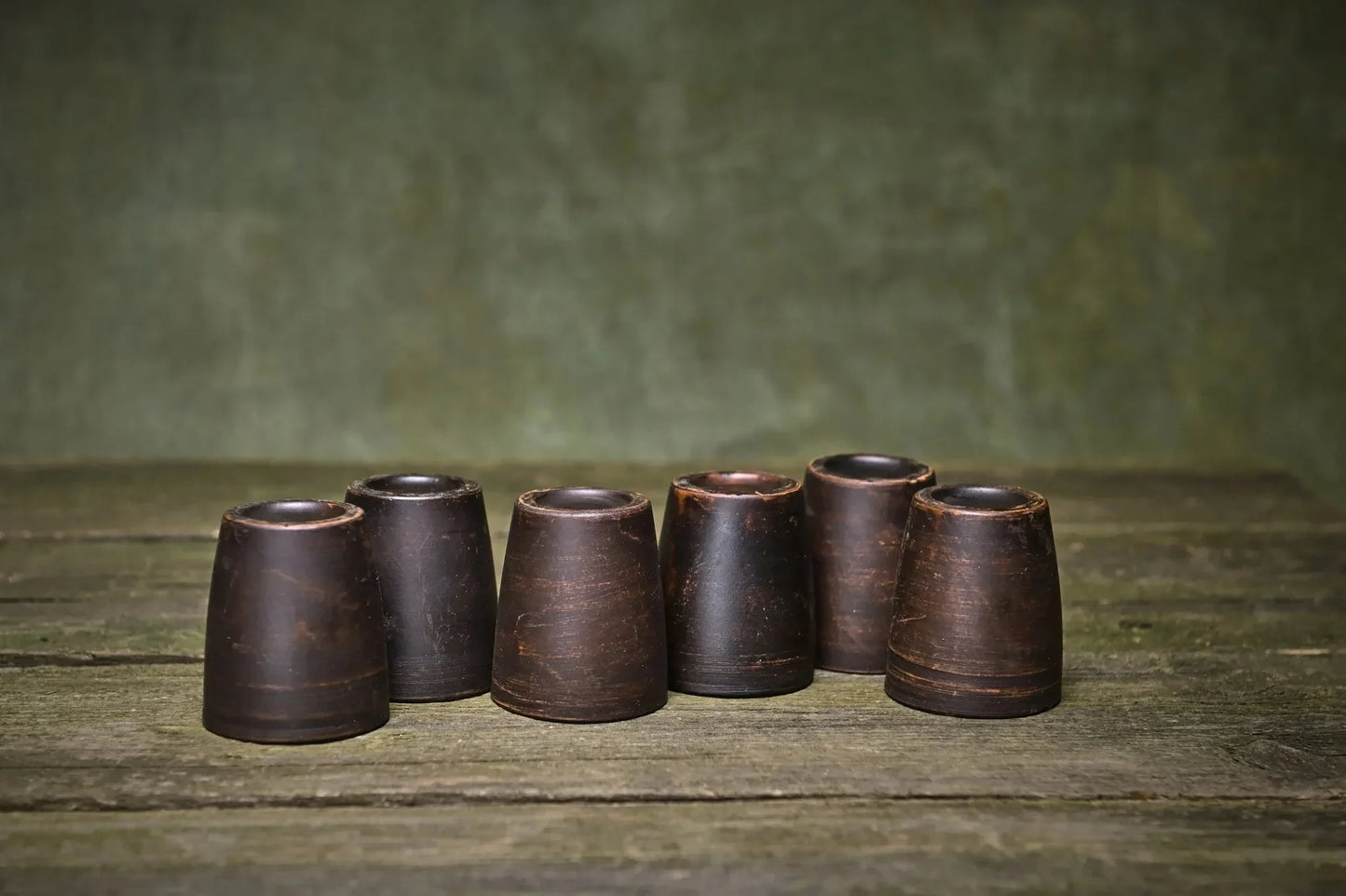 Set of 6 handmade dark brown ceramic shot glasses on rustic wooden surface