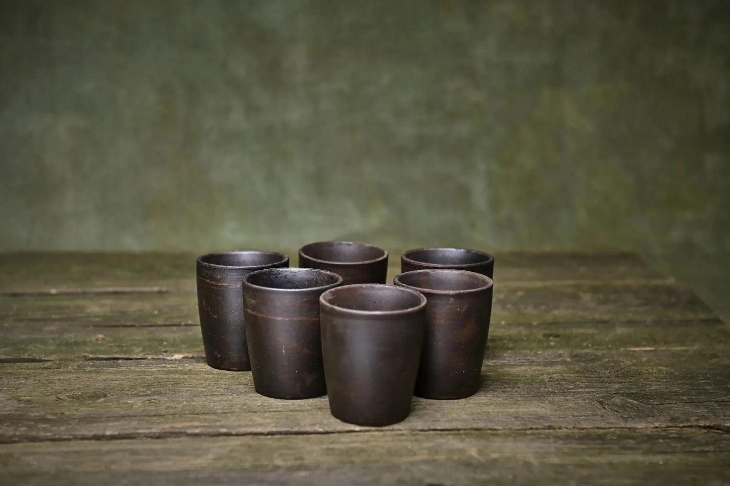 Set of 6 handmade ceramic shot glasses in dark clay on rustic wooden table