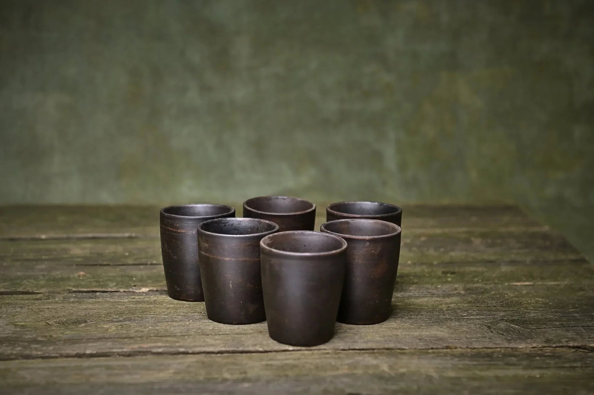 Set of 6 handmade ceramic shot glasses in dark clay on rustic wooden table