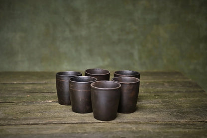 Set of 6 handmade ceramic shot glasses in dark clay on rustic wooden table