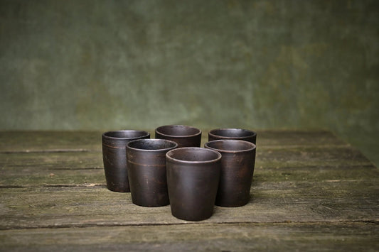 Set of 6 handmade ceramic shot glasses in dark clay on rustic wooden table