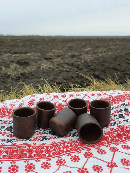 Set of six handmade clay shot glasses on embroidered cloth, artisan homeware decor
