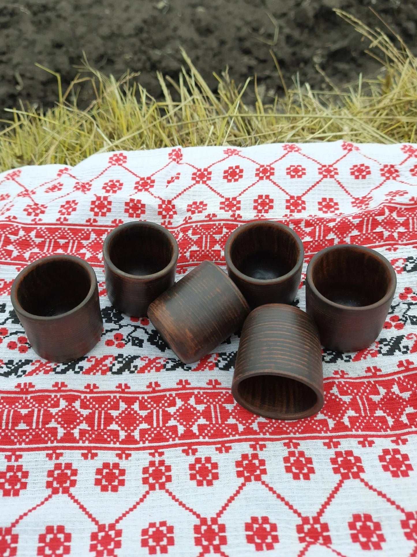 Set of six handmade clay shot glasses on embroidered cloth, rustic outdoor setting