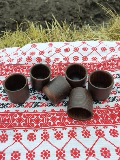 Set of six handmade clay shot glasses on embroidered cloth, rustic outdoor setting