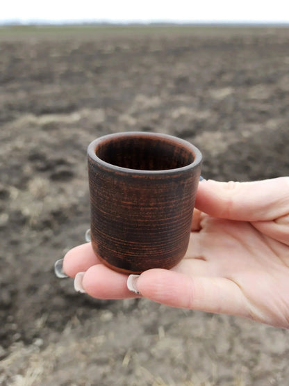 Hand holding a small handmade clay shot glass outdoors, rustic artisan ceramic homeware