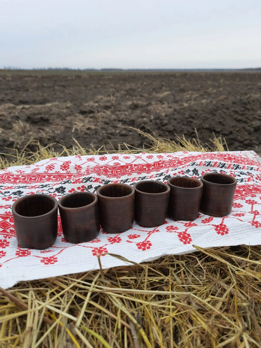 Set of six handmade clay shot glasses on embroidered cloth, rustic outdoor setting