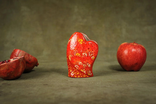 Hand-painted red ceramic heart-shaped vase with floral patterns, displayed with apple and pomegranate.