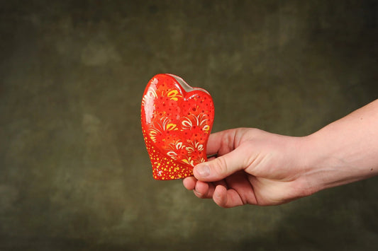 Hand holding a small, handcrafted red heart-shaped ceramic vase with floral patterns