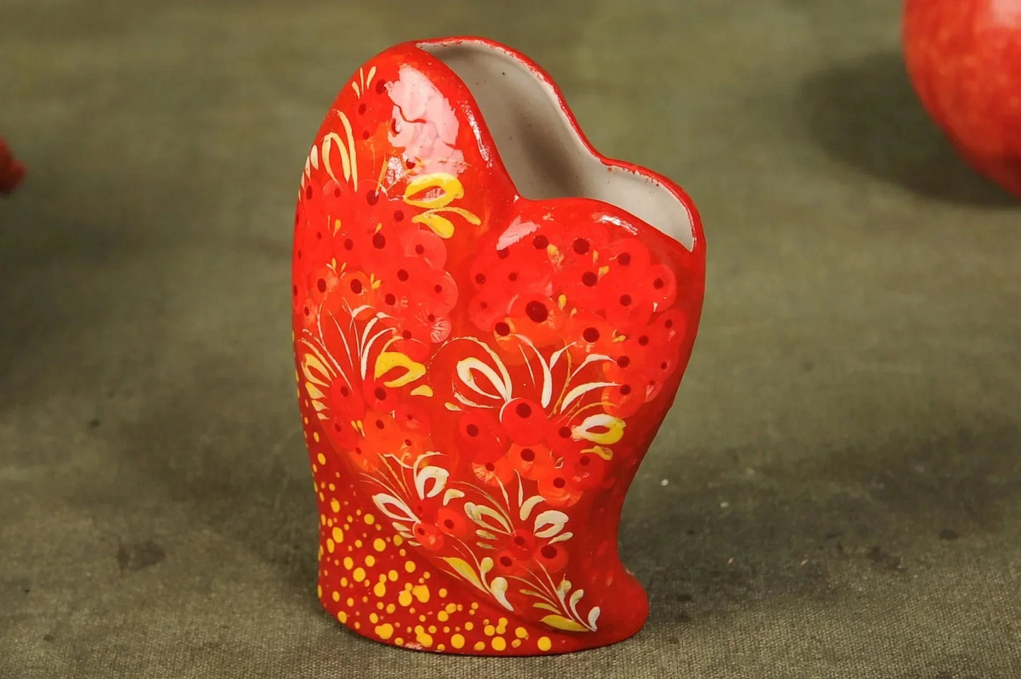 Handmade heart-shaped red ceramic vase with floral pattern on green surface, clay home decor
