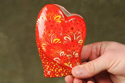 Hand holding a small red ceramic heart-shaped vase with yellow floral hand-painted design