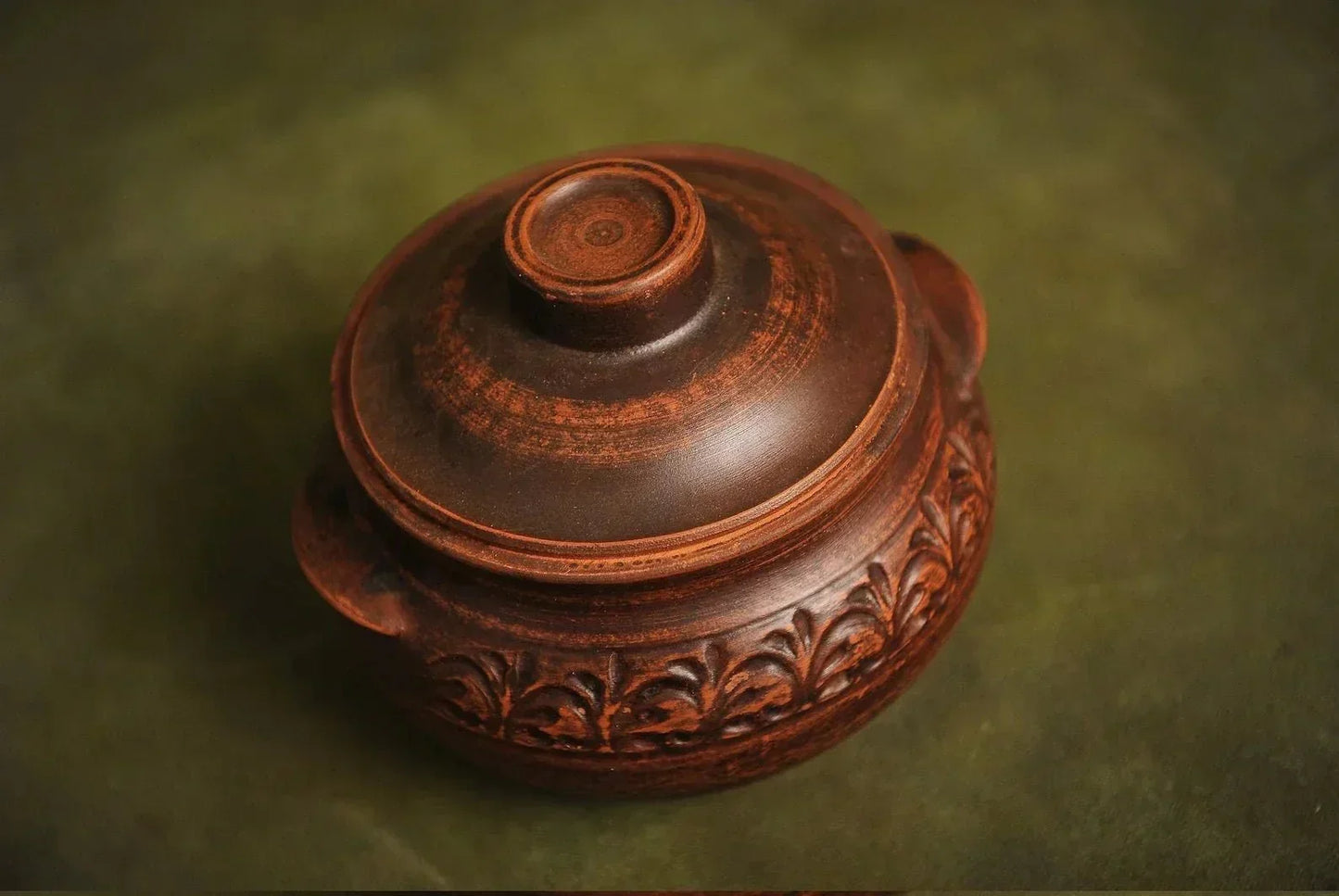 Handmade brown clay casserole dish with lid, artisan pottery on green background