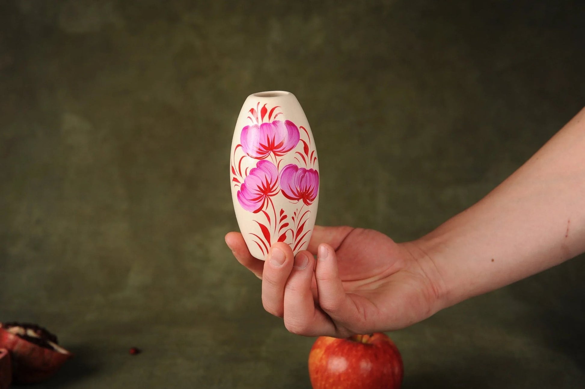 Hand holding a small handcrafted white ceramic vase with pink floral design, home decor