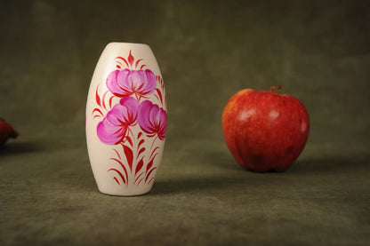 Hand-painted ceramic vase with pink and red floral design beside a red apple on green cloth