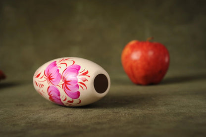 Hand-painted small ceramic vase with pink floral design, white clay, beside red apple