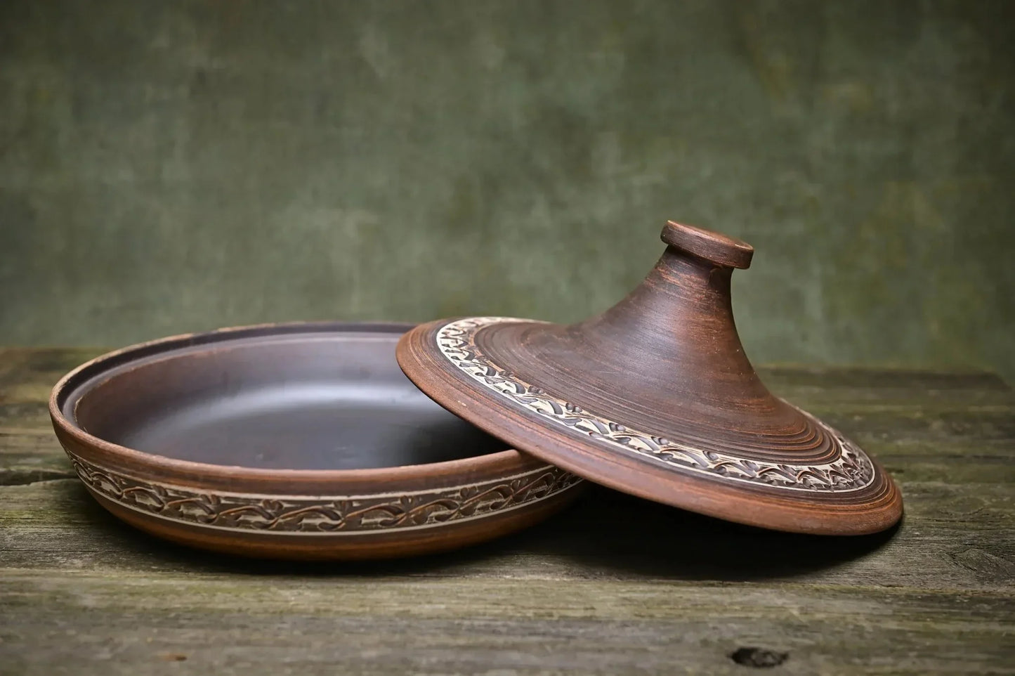 Handmade ceramic tagine clay cooking pot with decorative lid on rustic wood table