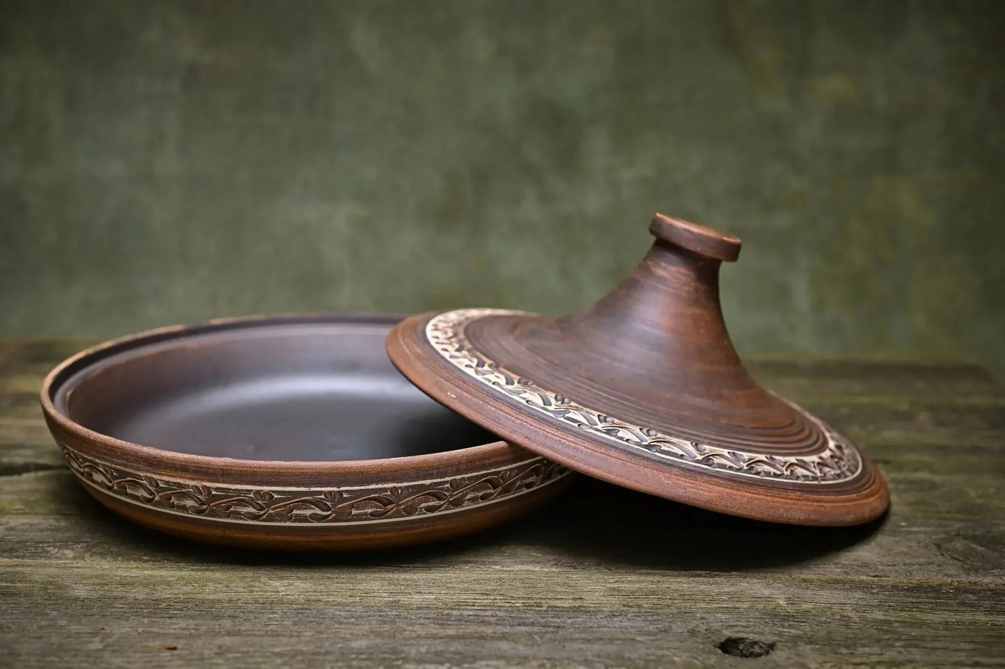 Handmade ceramic tagine clay pot with decorative lid on rustic wood surface
