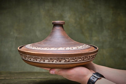 Handmade ceramic tagine pot with intricate pattern, held in hands, artisan clay cookware