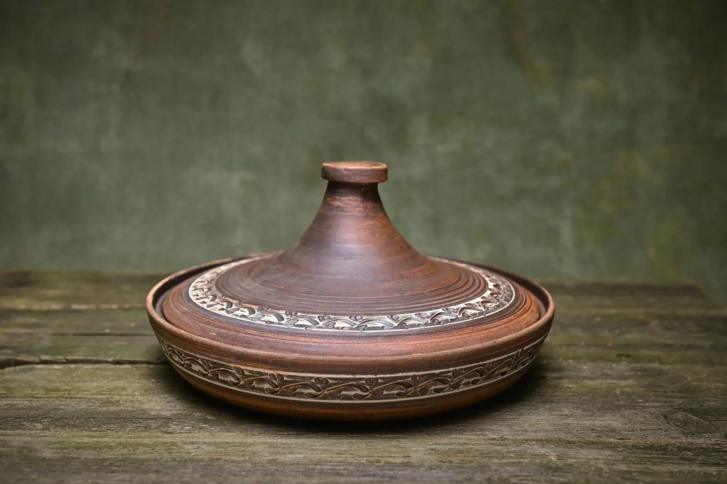 Handmade ceramic tagine pot with lid, decorative pattern, on rustic wood table