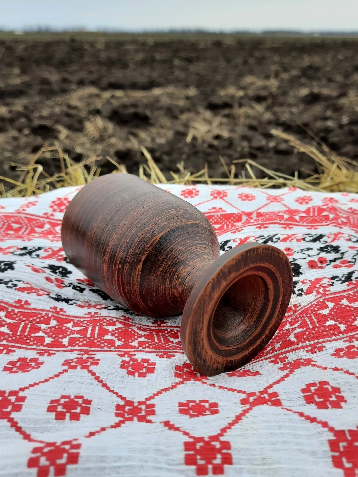 Handmade clay wine glass on embroidered cloth, artisan pottery homeware outdoors